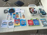 Video game cases and two bins with assorted figures and cards on table.