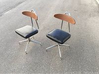 Two mid-century style chairs with chrome legs, black vinyl seats, and wooden backrests shown together on asphalt.