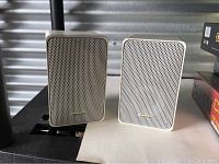 Front view of two white Realistic Minimus 7 speakers showing metal grills and branding.