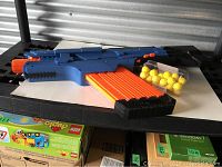 Blue Nerf Rival MXVI-4000 blaster with orange muzzle and orange clip, yellow foam balls in clear container on white background