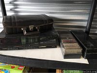 Photo showing Pioneer dual cassette deck with black carrying case on top, a plastic cassette tape storage box, and other metal storage case on side.