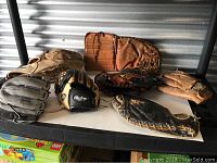 All seven baseball gloves arranged on a table showing variety of vintage and newer gloves.