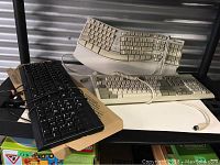Six used computer keyboards stacked and displayed showing different sizes and colors including black and beige, some with cables attached.