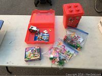 Four LEGO sets and two red LEGO storage containers on table, includes sealed LEGO Friends 41031 box and various pieces in plastic bags