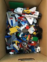 Top view of cardboard box containing assorted LEGO pieces and a partially assembled space shuttle model on top.