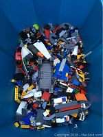 Top-down view of bin with assorted LEGO pieces including bricks, wheels, plates, and specialized parts