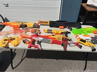 Wide view showing entire assortment of Nerf guns on a white table outdoors