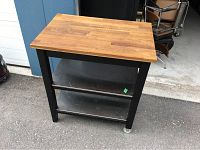 Front view showing butcher block top, two metal shelves and black frame
