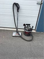 Full view of the vacuum cleaner showing the canister, hose, and floor head on the ground.