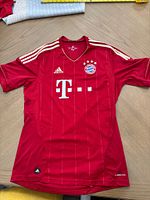 Front view of red Adidas FC Bayern Munich jersey showing sponsor logo and shoulder stripes