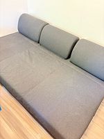 Overall view of sofa bed in flat position, showing gray upholstery and three back cushions