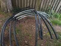 Curved galvanized frame tubes and black vertical enclosure poles on ground