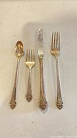 Four pieces of silver plated flatware laid out – teaspoon, salad fork, dinner knife, dinner fork