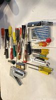 Top-down view of entire lot laid out on white table showing staple gun, screwdrivers, precision set, chisel, punches, staples and wrenches