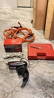 Lot overview showing booster cables, emergency light box, red tool case, glue gun, small metal tool and cords