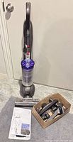 Dyson DC42 vacuum standing upright, box of attachments and manual visible