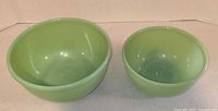 Two jadeite glass mixing bowls side by side, larger on left