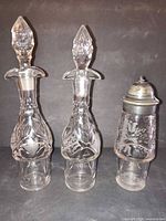 Front view of two cut glass decanters with stoppers and etched glass shaker with metal lid