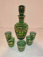 Full view of green glass decanter with stopper and four of six glasses