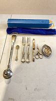 Full layout of candle snuffer, souvenir spoon, two forks, knife, stork scissors, decorative dish and packaging