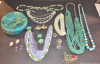 All jewellery items laid out including necklaces, earrings, brooch, ring and brocade tin