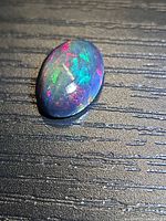 Oval cabochon opal on textured surface, showing multicolour play