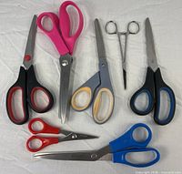 All seven scissors and locking tweezer displayed on fabric background