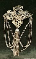 Front view showing filigree brooch, black cabochon, faux pearl, draped chains and tassel