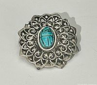 Front view of silver-tone filigree brooch showing turquoise scarab cabochon