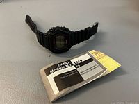 Black Casio digital wristwatch with instruction booklet and warranty leaflet displayed on surface