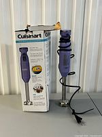 Hand blender standing next to its opened retail box on table