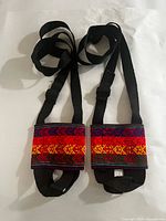 Pair of multicolour Peruvian textile water bottle holders with black straps displayed flat
