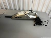 Full view of silver Oreck XL Auto handheld car vacuum with attached crevice tool and 12 V cord