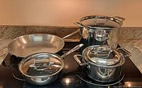 Four stainless pans and three lids on stovetop