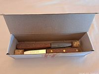 Two paring knives in cardboard box, corks on blade tips