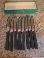 Eight steak knives lined beside green box lid removed