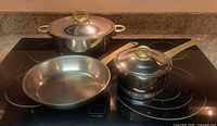 Three pieces of Kuhn Rikon Durotherm cookware on stovetop: stockpot with lid, saucepan with lid, frying pan