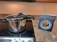 Pressure cooker on stove beside cookbook front cover