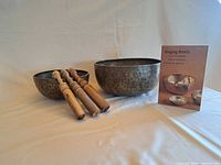 Two metal singing bowls with three wooden strikers and guide book