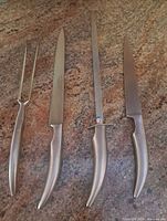 Four stainless steel utensils laid out: carving fork, fillet knife, honing file, carving knife