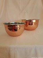 Two polished copper exterior, stainless interior mixing bowls side by side