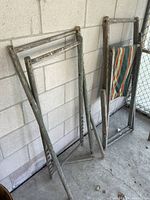 Two folding wooden lawn chair frames leaning against wall; one retains coloured canvas, other missing canvas