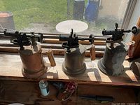 Three brass blow torches side by side on windowsill