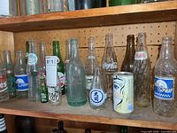 Shelf with assortment of vintage glass soda bottles and one soda can
