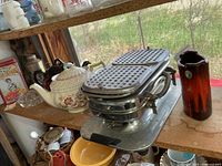 Shelf view showing waffle maker, floral teapot, pottery vase and additional items