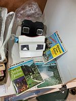 White GAF View-Master viewer stacked on black viewer with three reel packets visible
