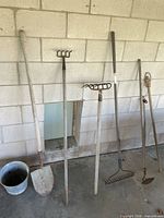 Group of long-handled yard tools leaning against wall