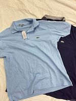 Light blue and navy Lacoste polo shirts side by side