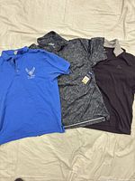 Three polo shirts laid out side by side: blue USAF, black speckled with tag, charcoal with grey collar