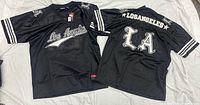 Front and back views of both black Shekinah Los Angeles jerseys